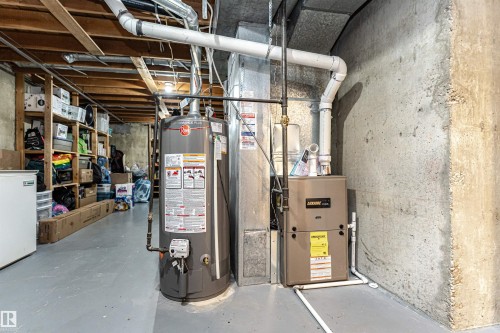 Dedicated utility area featuring a water heater and furnace, exposed ceiling joists, and concrete walls - 17716 84 Ave, Edmonton, AB - Indoor Photo Showing Basement