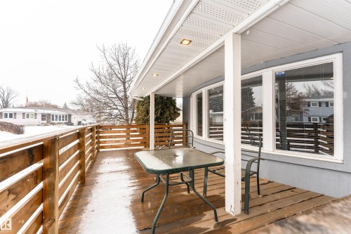 Expansive covered deck featuring natural wood decking and a slatted wood-finish railing - 17716 84 Ave, Edmonton, AB - Outdoor With Deck Patio Veranda