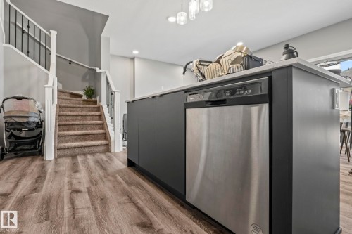 Modern kitchen island with a stainless steel dishwasher, light-toned countertop, and dark cabinetry - 5142 23A Avenue, Edmonton, AB - Indoor