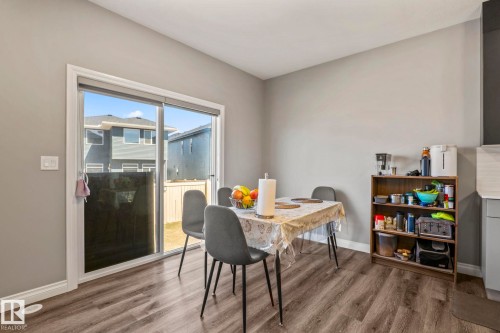 Dining area featuring wood-finish flooring, light gray walls, white baseboards, and a glass sliding door - 5142 23A Avenue, Edmonton, AB - Indoor Photo Showing Dining Room