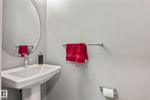 Pedestal sink with chrome faucet, complemented by a round wall-mounted mirror - 5142 23A Avenue, Edmonton, AB - Indoor Photo Showing Bathroom