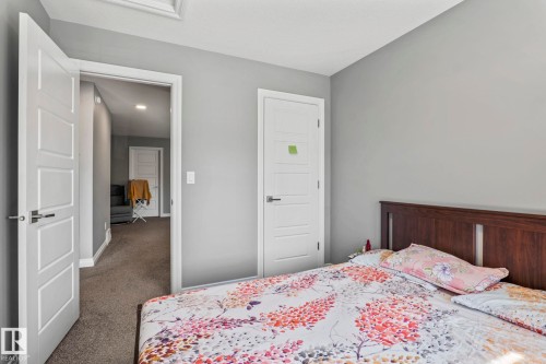 Bedroom featuring light gray wall paint, dark wood-finish headboard, and white paneled doors with contemporary hardware - 5142 23A Avenue, Edmonton, AB - Indoor Photo Showing Bedroom