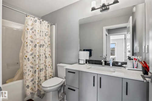 Bathroom featuring a white tub with shower, contemporary vanity with a white countertop, integrated sink, and an expansive wall mirror - 5142 23A Avenue, Edmonton, AB - Indoor Photo Showing Bathroom
