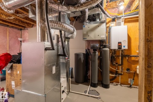 Utility area featuring a forced-air furnace, tankless water heater, water softener system, and exposed ceiling joists - 5142 23A Avenue, Edmonton, AB - Indoor Photo Showing Basement