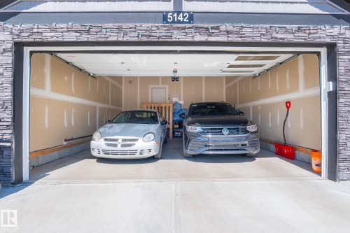 Two-car garage featuring a concrete floor, unpainted drywall, and a stacked stone exterior accent - 5142 23A Avenue, Edmonton, AB -  Photo Showing Garage