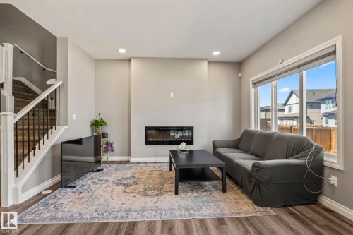 Living room featuring wood-finish flooring, a contemporary fireplace, and a large window - 5142 23A Avenue, Edmonton, AB - Indoor With Fireplace