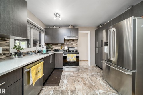 Kitchen featuring dark wood-finish cabinetry, stainless steel appliances, white countertops, and a mosaic tile backsplash - 14808 96 Street, Edmonton, AB - Indoor Photo Showing Kitchen With Double Sink