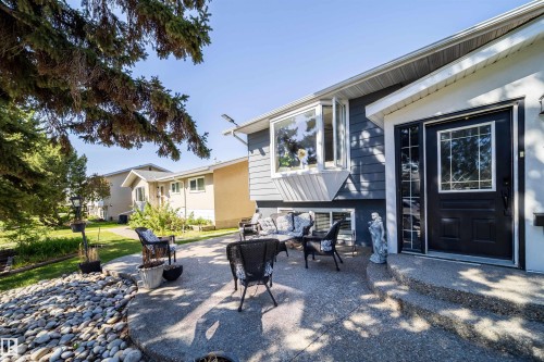 Exterior featuring a dark-paneled front door with decorative glass, a prominent bay window, light gray siding, and a concrete patio with an integrated rock garden - 14808 96 Street, Edmonton, AB - Outdoor