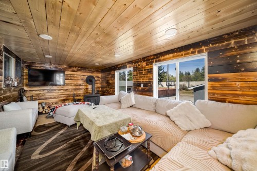 Wood-paneled living space featuring a wood-burning stove with an exposed flue, multiple windows, recessed ceiling lights, and wood-finish flooring - 14808 96 Street, Edmonton, AB - Indoor