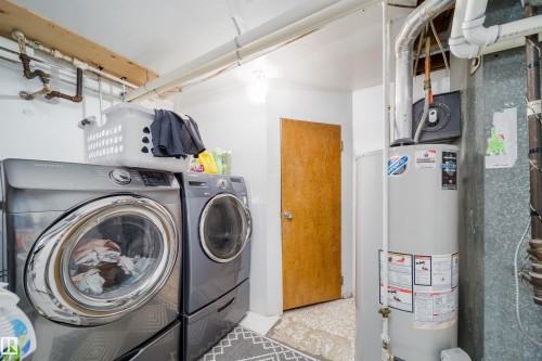 Dedicated laundry area featuring a front-loading washer and dryer, exposed overhead piping, and a water heater - 14808 96 Street, Edmonton, AB - Indoor Photo Showing Laundry Room