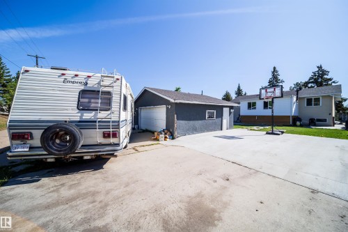 Detached garage with a roll-up door and a side entry, alongside a spacious concrete driveway and concrete patio space - 14808 96 Street, Edmonton, AB - Outdoor