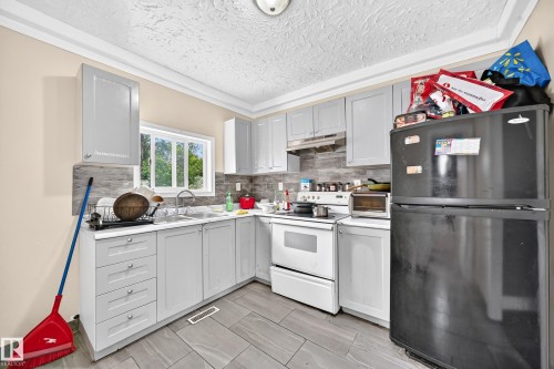 Kitchen featuring light gray cabinetry, white countertops, a stainless steel sink, and a tile backsplash - 12627 71 Street Nw, Edmonton, AB 