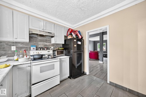 Kitchen featuring white cabinetry, a tile backsplash, a range with an overhead hood, and gray tiled flooring - 12627 71 Street Nw, Edmonton, AB 