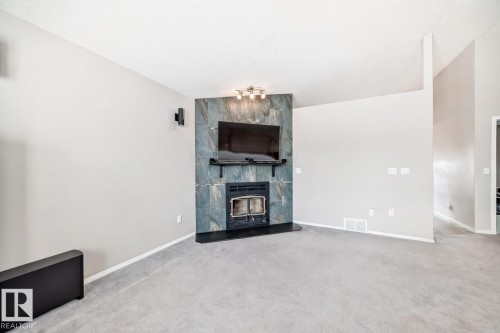 Living area featuring light grey walls, light grey carpet flooring, and a fireplace with a dark grey stone surround and a black hearth - 8008 97 St, Morinville, AB - Indoor With Fireplace