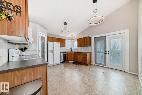 The kitchen features wooden cabinetry, light-toned tile flooring, and a vaulted ceiling with contemporary light fixtures - 8008 97 St, Morinville, AB - Indoor Photo Showing Kitchen