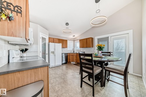 This kitchen features wood cabinetry, white appliances, and a tiled backsplash - 8008 97 St, Morinville, AB - Indoor