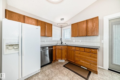 The kitchen features wood cabinetry, a white side-by-side refrigerator, a stainless steel dishwasher, and tile flooring - 8008 97 St, Morinville, AB - Indoor Photo Showing Kitchen
