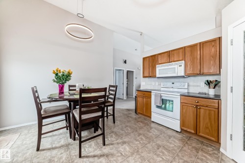 This open-concept area features vaulted ceilings, tile flooring, and a kitchen with wood cabinetry, white appliances, and a tiled backsplash - 8008 97 St, Morinville, AB - Indoor