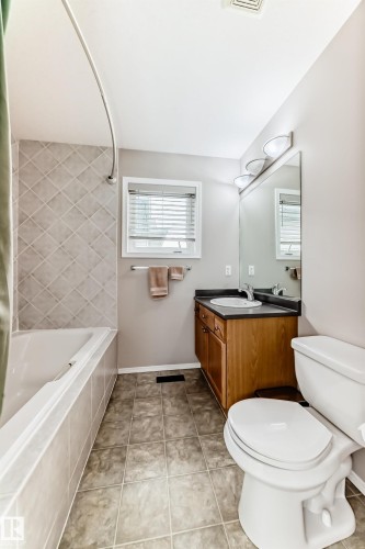 The bathroom features a vanity with a wood-toned cabinet and a dark countertop, a toilet, and a bathtub with tiled surround - 8008 97 St, Morinville, AB - Indoor Photo Showing Bathroom