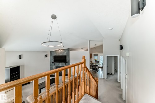 The property features a staircase with wooden railings, a spacious living area with a stone-clad fireplace, and a dining area visible through an opening - 8008 97 St, Morinville, AB - Indoor Photo Showing Other Room