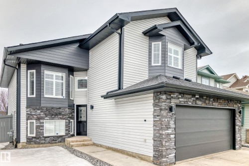 The property features a two-story exterior with light-colored siding, dark gray accents, and stone detailing around the garage and bay windows - 8008 97 St, Morinville, AB - Outdoor