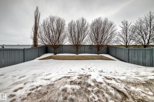 The property features a fenced yard with a retaining wall and several mature trees - 8008 97 St, Morinville, AB - Outdoor