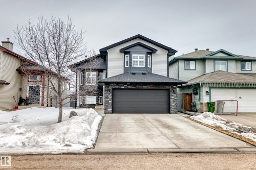 The property features a dark grey garage door framed by stone cladding, a concrete driveway, and light grey siding with dark grey trim - 8008 97 St, Morinville, AB - Outdoor With Facade
