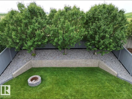 The property features a well-maintained lawn, a stone fire pit, and a gravel bed with mature trees, all enclosed by a privacy fence - 8008 97 St, Morinville, AB - Outdoor