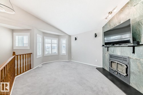 Spacious living area featuring light gray carpeting, a decorative stone fireplace, and a bay window with plantation shutters - 8008 97 St, Morinville, AB - Indoor Photo Showing Other Room With Fireplace