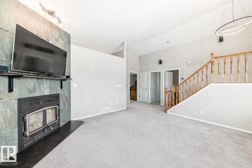 Spacious living area featuring light gray carpeting, a natural stone fireplace with a black hearth, and a wooden staircase with balusters - 8008 97 St, Morinville, AB - Indoor With Fireplace