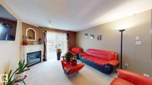 Living room featuring a fireplace with a white mantel, sliding glass door, light-colored carpet, and an accent wall - 405 16303 95 Street Nw, Edmonton, AB - Indoor Photo Showing Living Room With Fireplace