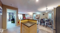 Kitchen peninsula with a dark countertop and integrated cabinetry, stainless steel refrigerator, and recessed lighting - 