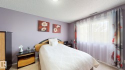 Bedroom featuring a wide window with sheer and patterned drapes, a textured ceiling, and light-colored flooring - 