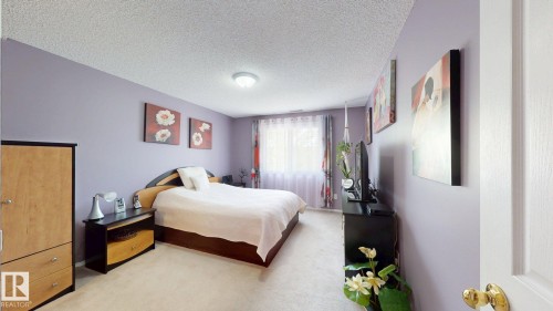 Spacious bedroom featuring light lavender walls, plush carpet flooring, a large window with sheer and patterned curtains, and a ceiling-mounted light fixture - 405 16303 95 Street Nw, Edmonton, AB - Indoor Photo Showing Bedroom