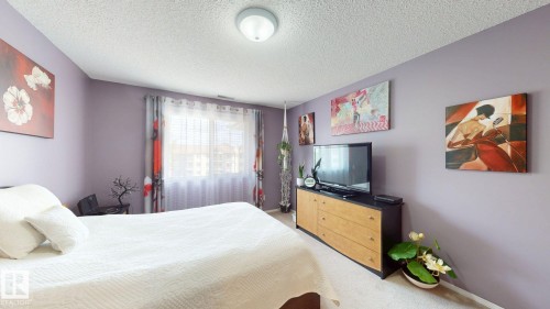 Carpeted room featuring light purple walls, a single window with blinds and floral curtains, and a ceiling-mounted light fixture - 405 16303 95 Street Nw, Edmonton, AB - Indoor Photo Showing Bedroom