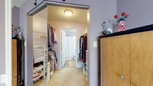 Walk-through closet featuring mirrored sliding doors, wire shelving, and built-in wood-finish cabinetry - 405 16303 95 Street Nw, Edmonton, AB - Indoor Photo Showing Other Room