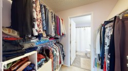 Walk-in closet featuring built-in shelving, multiple hanging rods, and direct access to an adjacent bathroom with a white shower curtain and toilet - 