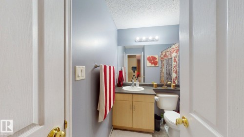 Bathroom featuring a light wood-finish vanity with an integrated sink, a dark countertop, and a vanity mirror with overhead lighting - 405 16303 95 Street Nw, Edmonton, AB - Indoor Photo Showing Bathroom