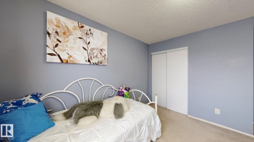 Bedroom featuring light blue walls, a textured ceiling, neutral carpet flooring, and a closet with white sliding doors - 405 16303 95 Street Nw, Edmonton, AB - Indoor Photo Showing Bedroom