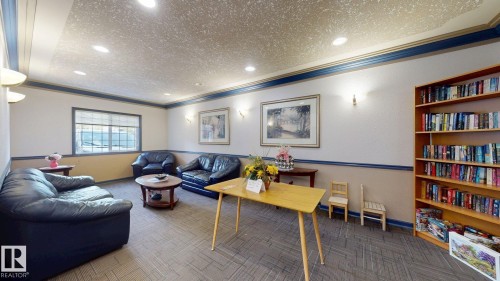 Spacious common area featuring textured carpeting, a large window with blinds, and built-in wall sconces - 405 16303 95 Street Nw, Edmonton, AB - Indoor