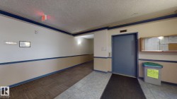 Elevator access in a common area featuring wall-mounted lighting, a display case, and mixed flooring with tile and patterned carpet - 
