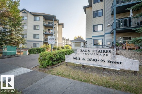 The Eaux Claires Promenade complex features multi-story residential buildings with individual balconies, a prominent stone monument sign, and a paved entranceway - 405 16303 95 Street Nw, Edmonton, AB - Outdoor With Balcony With Facade