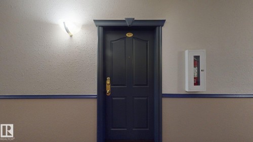 Painted door with gold-toned hardware, overhead wall sconce, and textured wall finish - 405 16303 95 Street Nw, Edmonton, AB -  Photo Showing Other Room
