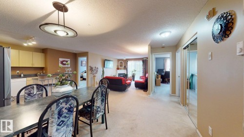 Open-concept living space featuring a dining area with an overhead pendant light, a kitchen with light-colored cabinetry and a breakfast bar, and a living room with a built-in fireplace - 405 16303 95 Street Nw, Edmonton, AB - Indoor Photo Showing Dining Room