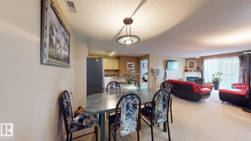 Open-concept living space featuring a dining area with pendant lighting, a kitchen with light wood cabinetry, a living room with a fireplace, and a glass sliding door - 405 16303 95 Street Nw, Edmonton, AB - Indoor Photo Showing Other Room