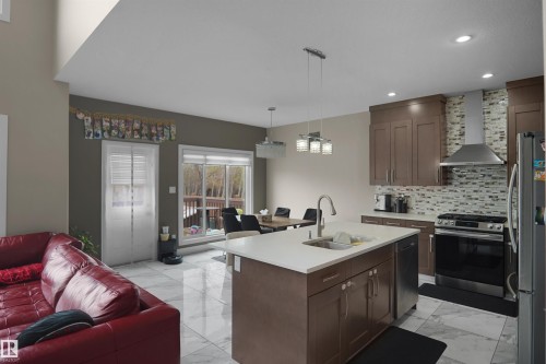Kitchen featuring a central island with an undermount sink and stainless steel faucet, brown cabinetry, mosaic tile backsplash, and stainless steel appliances - 6108 173 Ave, Edmonton, AB 