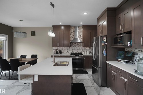 Modern kitchen featuring dark wood-finish cabinetry, stainless steel appliances, a tile backsplash, and light-toned countertops - 6108 173 Ave, Edmonton, AB 