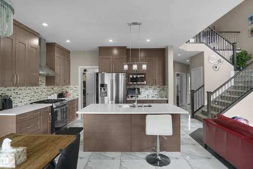Modern kitchen featuring a large central island with seating, stainless steel appliances, and a mosaic tile backsplash - 6108 173 Ave, Edmonton, AB 