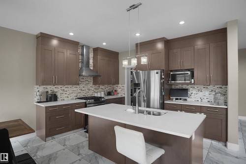 Contemporary kitchen featuring custom cabinetry, stainless steel appliances, a center island with sink, mosaic tile backsplash, and large format floor tiling - 6108 173 Ave, Edmonton, AB 