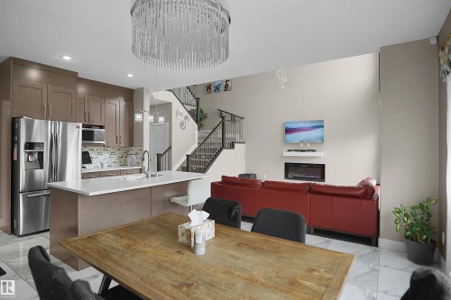 Open-concept living space featuring a modern kitchen with stainless steel appliances, a center island with seating, and a mosaic tile backsplash - 6108 173 Ave, Edmonton, AB 